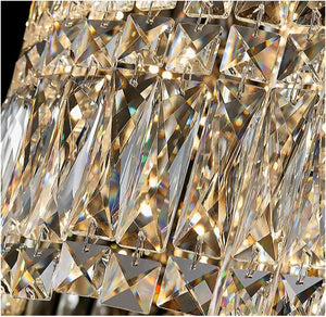 Close-up of a faceted crystal chandelier detail with multiple clear geometric prisms reflecting warm light and showing iridescent rainbow reflections.