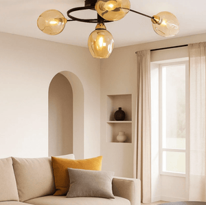 A modern multi-light ceiling fixture with five amber-tinted glass globes and a black metal frame, installed in a warm, minimalist living room with a beige sofa and window.