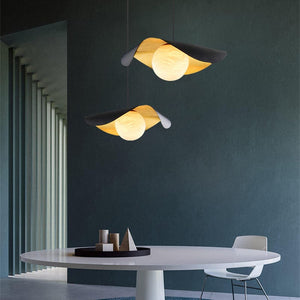 Two modern pendant lights with curved black and warm yellow-gold shades hang above a white dining table in a minimalist room with a dark teal wall.
