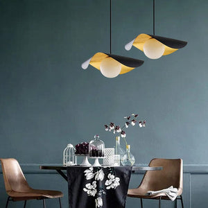 Two modern pendant lights with black and yellow flower-shaped shades hang above a dining table in a styled room with brown chairs and a dark blue-gray wall.