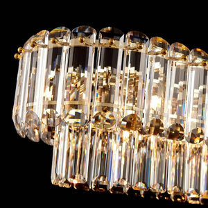 A close-up of a modern crystal chandelier featuring clear glass cylindrical tubes and gold-toned metal accents, photographed against a solid black background.