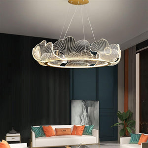 A modern circular pendant chandelier with a gold-toned metal frame and intricate wire filigree leaf-like designs, suspended in a contemporary living room setting.