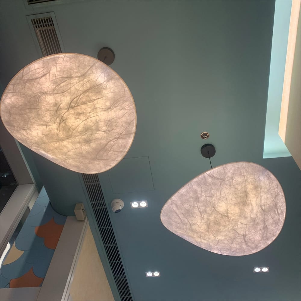 Two large organic-shaped pendant light fixtures with textured, translucent beige shades hanging from a light blue ceiling in an indoor space.
