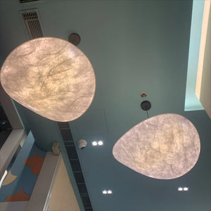 Two large organic-shaped pendant light fixtures with textured, translucent beige shades hanging from a light blue ceiling in an indoor space.