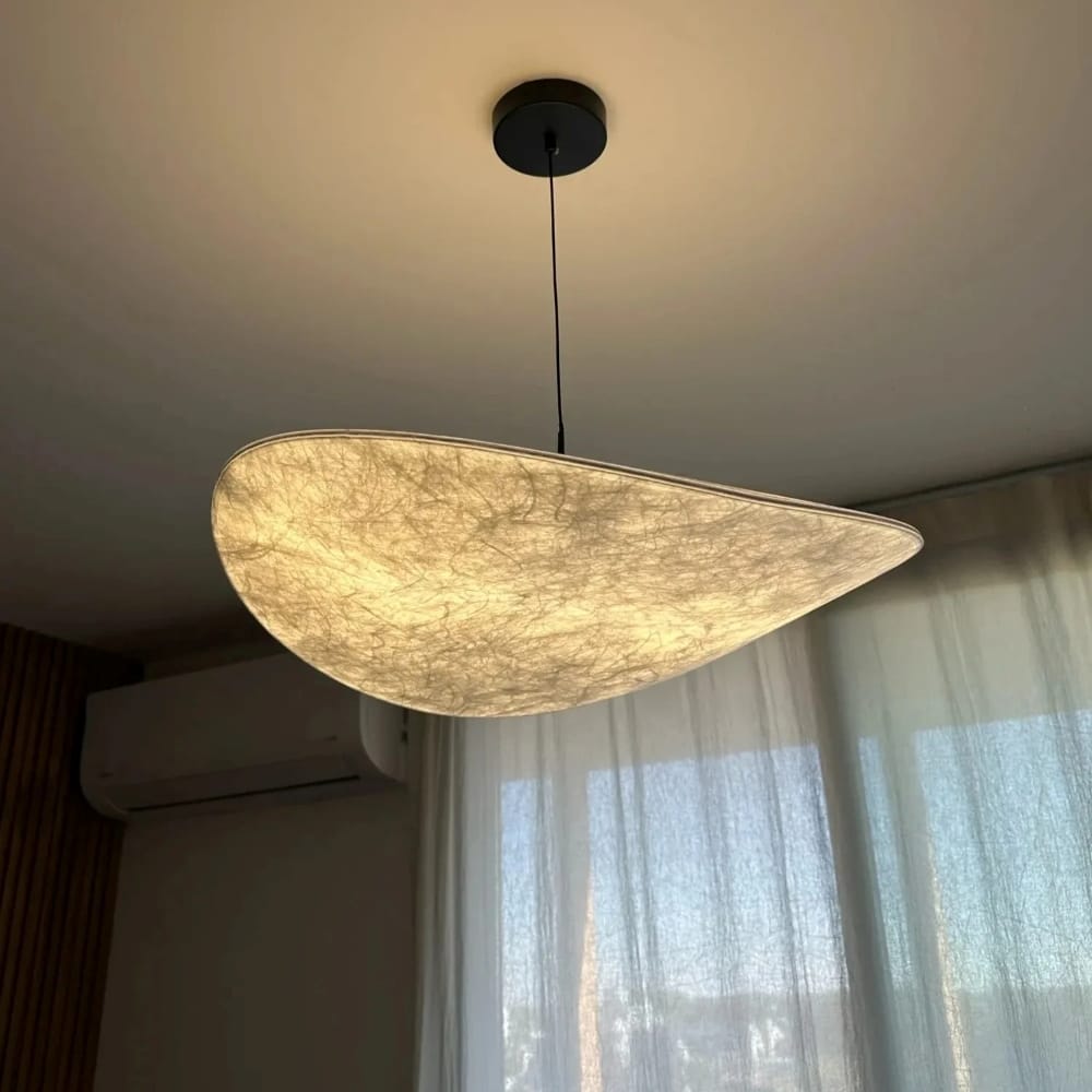 Modern pendant light hanging from the ceiling with a window and curtain in the background.