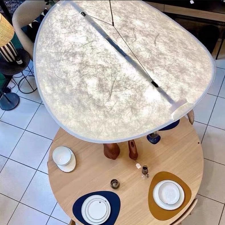 An overhead view of a large oval table lamp with a textured, marbled off-white shade, shown lit above a round wooden dining table in a room with tiled floors.