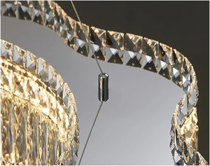 Close-up of a modern spiral chandelier with clear faceted crystal prisms and warm gold-toned lighting, suspended by thin cables with a central dark metal connector.