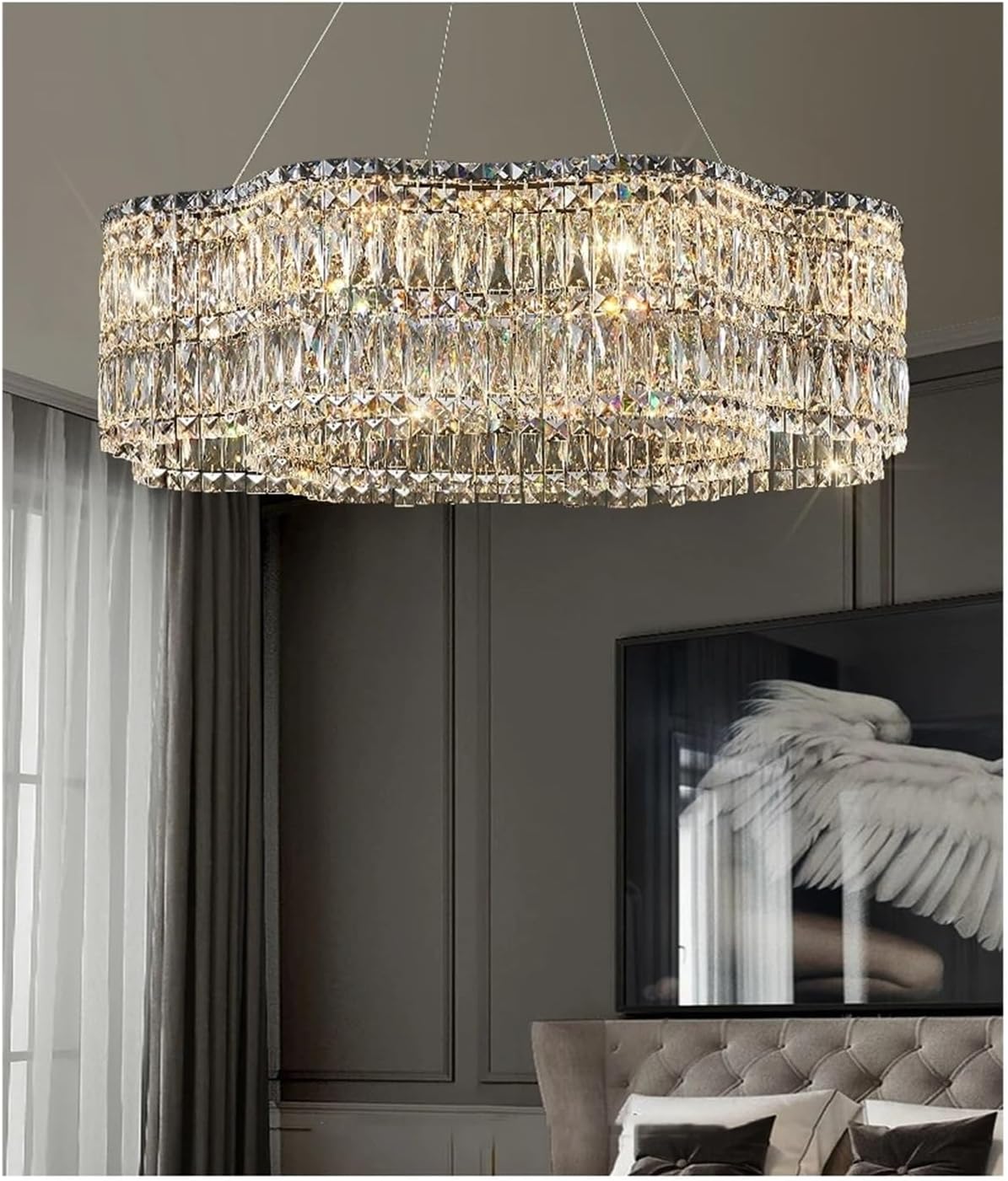 A large rectangular crystal chandelier with cascading clear glass and crystal prisms, illuminated in a modern bedroom setting with gray walls and a tufted headboard.