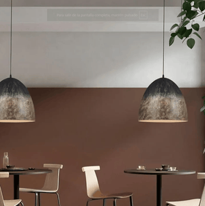 Two dome-shaped pendant lights with a distressed black and bronze finish hang over a dining area with tables and chairs against a two-tone brown and gray wall.