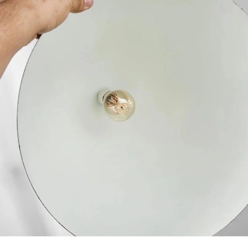 A close-up of a hand holding the edge of a large, round, off-white ceiling light fixture, showing a clear glass globe bulb with a warm filament at the center.