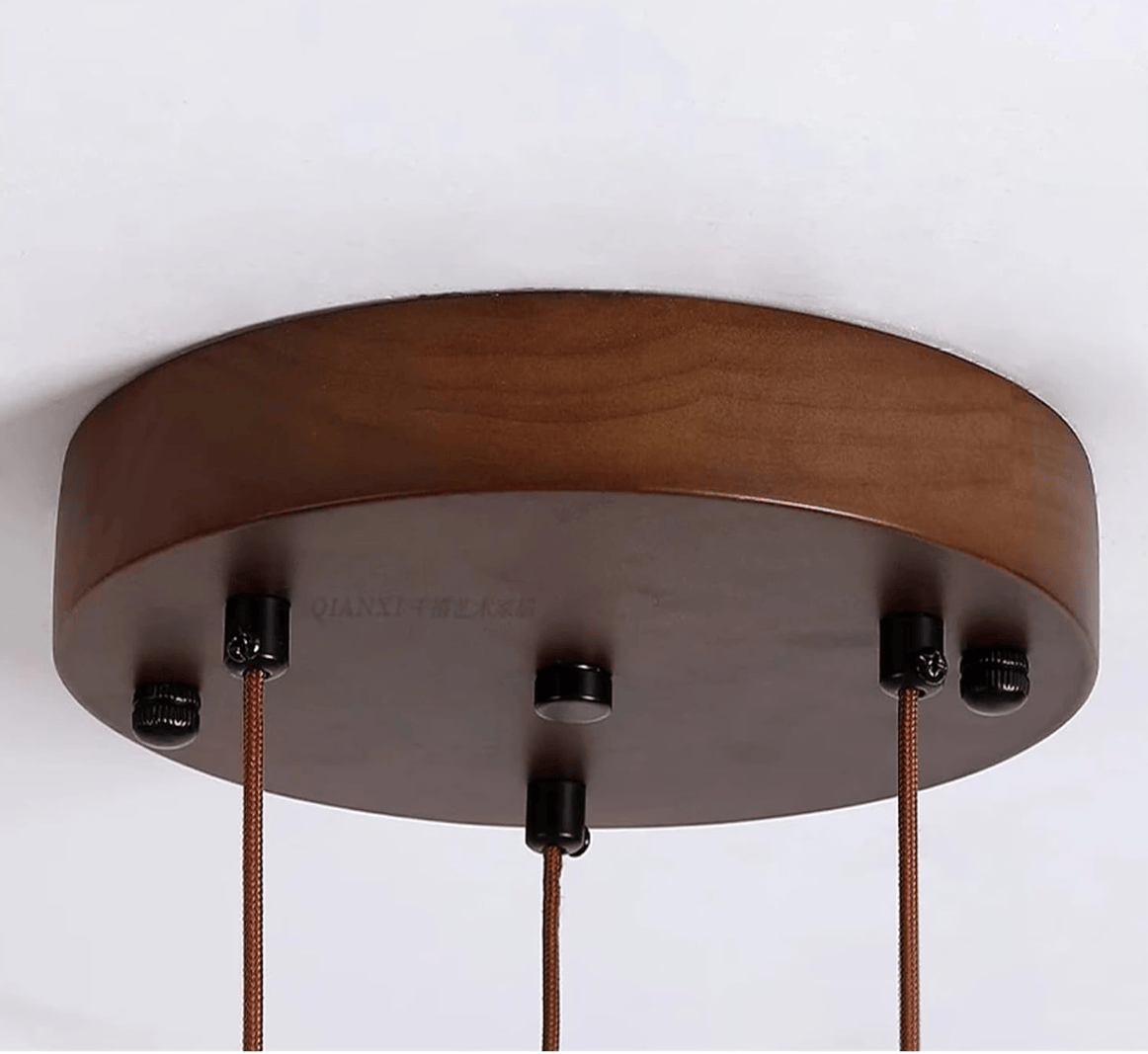A close-up of a round wooden ceiling canopy with three hanging cords attached by black hardware, shown against a plain white background.
