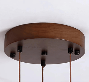 A close-up of a round wooden ceiling canopy with three hanging cords attached by black hardware, shown against a plain white background.