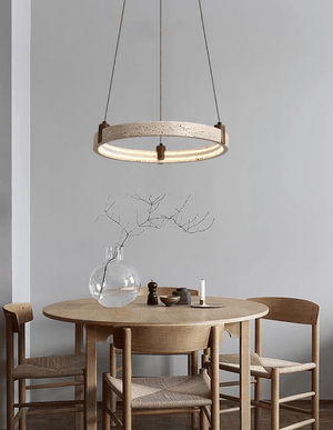 A modern circular pendant light with a light wood ring and warm glowing LED bulbs, hanging above a round wooden dining table with woven chair seats in a minimalist dining room.