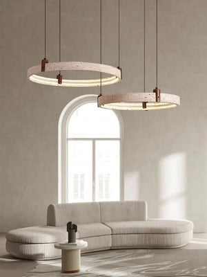 Two modern circular pendant lights with textured beige stone-like rings and dark metal accents, hanging in a minimalist living room with a curved light beige sofa and a bright arched window.