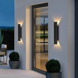 Modern outdoor wall lights on a white wall with a glass door and plants.