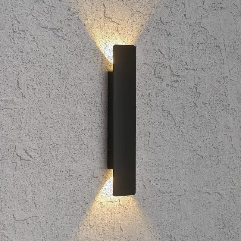 A modern matte black rectangular wall sconce mounted on a textured white stucco wall, casting a warm yellow light upward and downward.