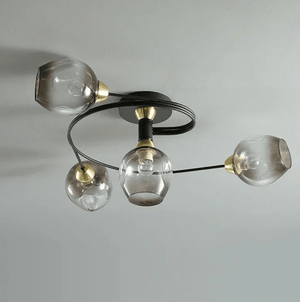 Modern three-light ceiling fixture with clear smoked glass globes, a curved black metal arm, and gold-toned accents on a plain light gray ceiling.