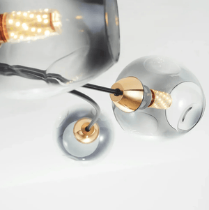 Modern glass pendant light fixture with a clear glass globe shade, black cord, and brushed brass metal socket, shown against a white background.