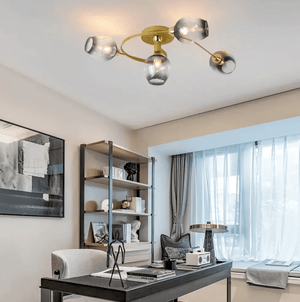 Modern ceiling light fixture with a gold central body and four clear glass shades, mounted on a ceiling in a styled home office interior.