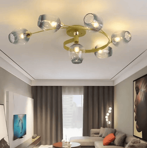 Modern ceiling light fixture with six translucent smoky glass shades on a curved gold metal frame, installed in a contemporary living room.