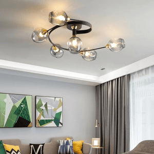 Modern ceiling light fixture with six clear glass globes on a curved black metal frame with gold accents, installed in a contemporary living room with gray walls, abstract art, and curtains.