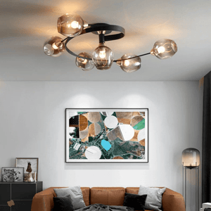 A modern multi-light ceiling fixture with six clear glass globes and a black circular frame, mounted on the ceiling in a contemporary living room above a brown leather sofa and framed abstract wall art.