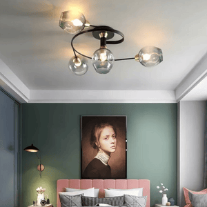 Modern ceiling light fixture with four clear glass globes and a black curved frame, installed in a bedroom with a green wall and pink bed.