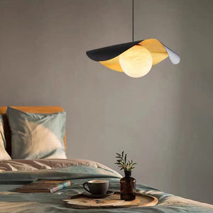 Modern pendant light hanging above a bed with a cup and plant on a tray.