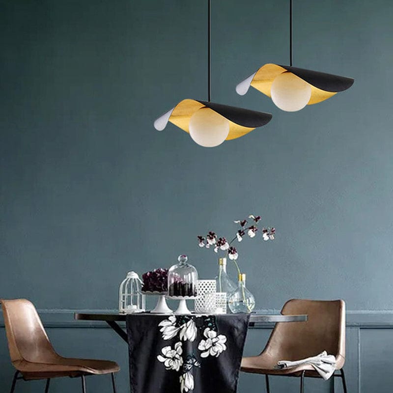 Two modern pendant lights with black and yellow flower-shaped shades hang above a dining table in a styled room with brown chairs and a dark blue-gray wall.