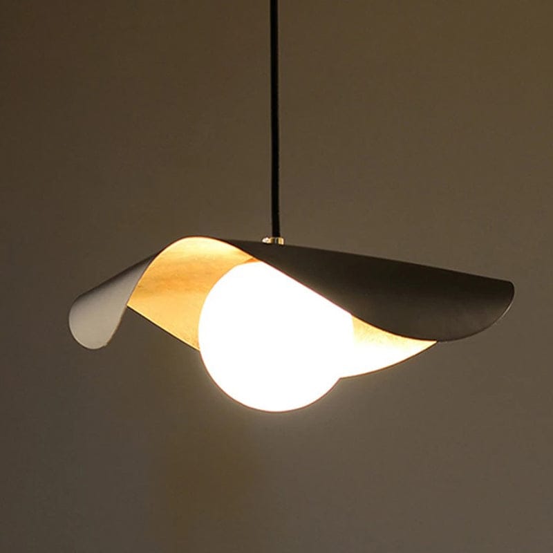 A modern pendant light with a curved black metal shade, a warm gold inner accent, and a glowing white spherical bulb, suspended against a plain taupe background.