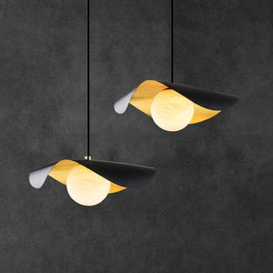 Two modern pendant lights with curved black and gold leaf-like shades and glowing round white bulbs, hanging against a dark textured wall.