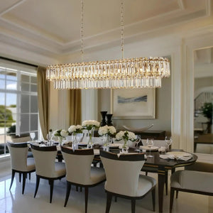A large rectangular crystal chandelier with hanging clear glass rods and gold-toned frame details, suspended over a dining table in a bright, elegant dining room.