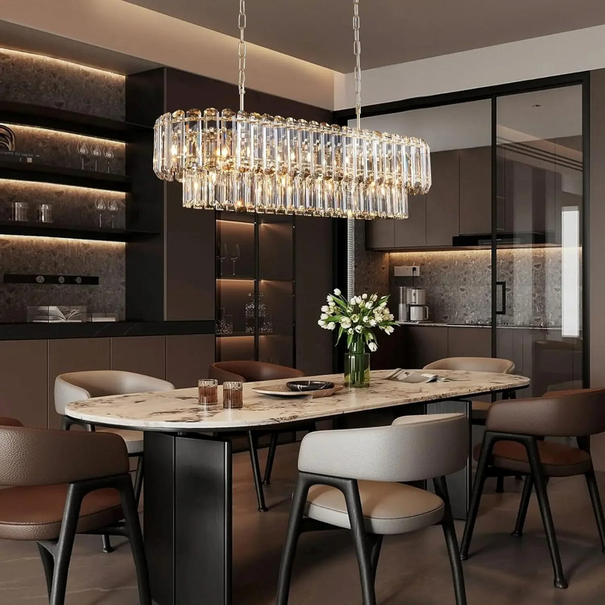 A modern rectangular crystal chandelier with clear hanging prisms and warm illuminated bulbs, suspended over a dining table in a contemporary kitchen-dining interior.
