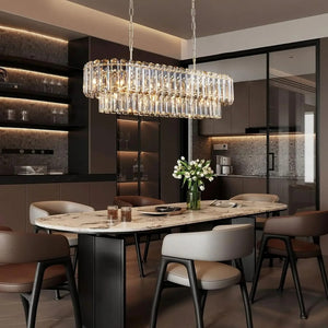 A modern rectangular crystal chandelier with clear hanging prisms and warm illuminated bulbs, suspended over a dining table in a contemporary kitchen-dining interior.