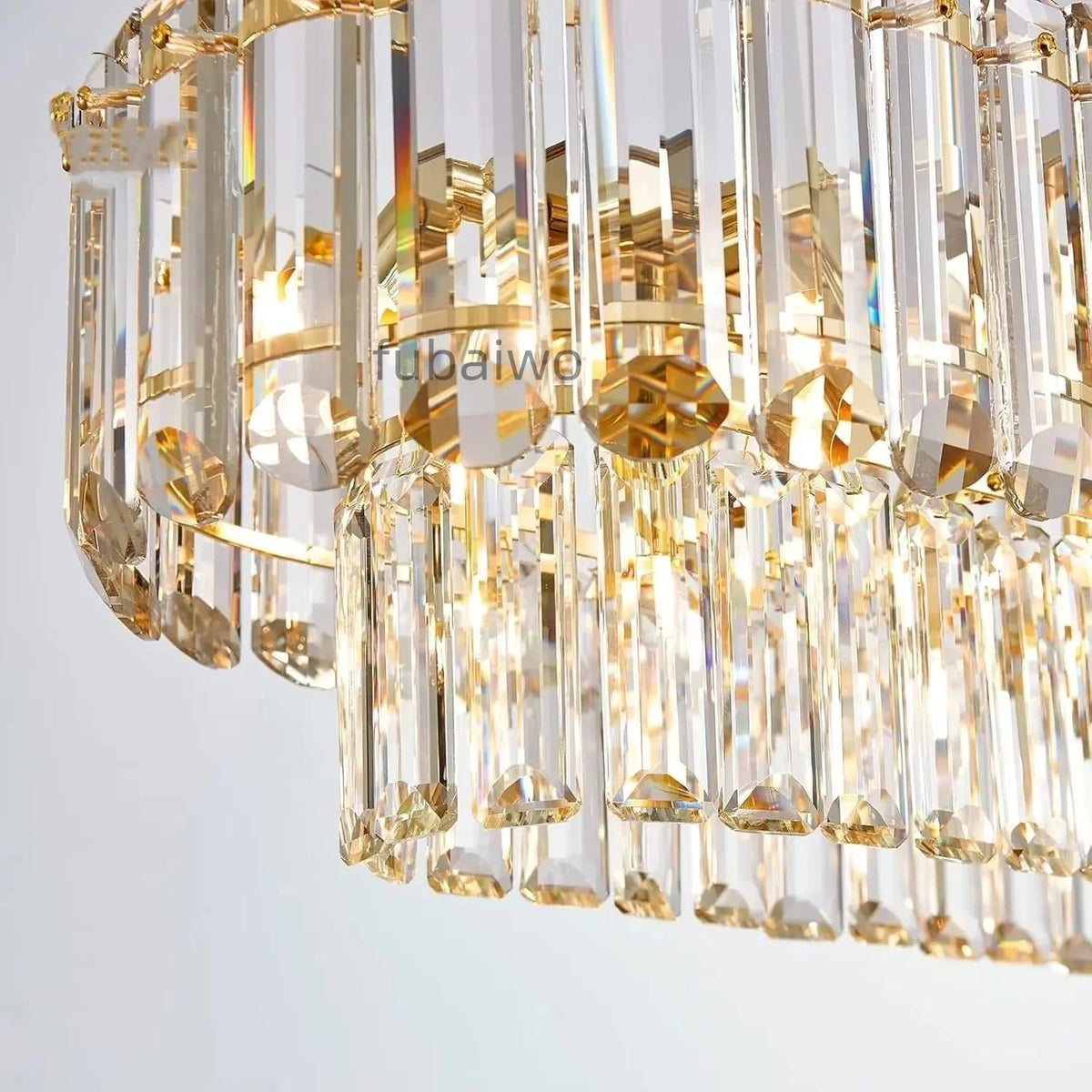Close-up of a modern crystal chandelier with clear faceted glass rods and gold-toned metal accents, shown against a light neutral background.