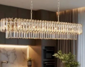 A modern rectangular chandelier with clear hanging glass rods and warm illuminated bulbs, shown hanging in a contemporary kitchen interior.