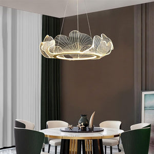 A modern flower-shaped LED pendant chandelier with a warm glowing light, suspended in a contemporary dining room setting with a round marble-top table and dark green chairs.