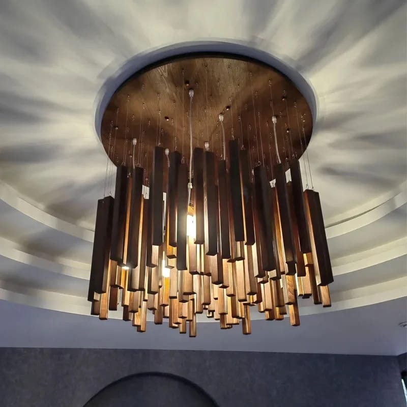 A modern multi-tiered chandelier with dark brown and bronze cylindrical rods, suspended from a round wooden ceiling plate in a curved white ceiling.