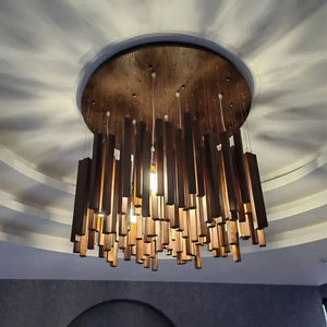 A modern multi-tiered chandelier with dark brown and bronze cylindrical rods, suspended from a round wooden ceiling plate in a curved white ceiling.